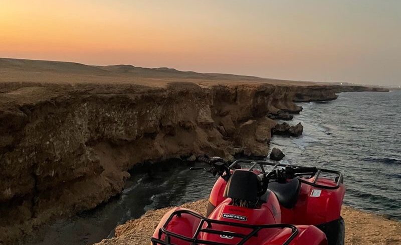 Quad rouge arrêté au bord de la falaise de Makadi, face à la mer Rouge au coucher du soleil