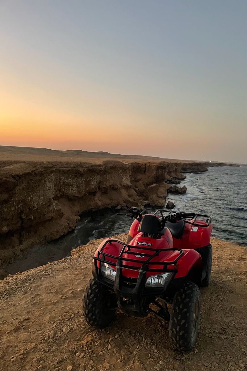Quad rouge arrêté au bord de la falaise de Makadi, face à la mer Rouge au coucher du soleil